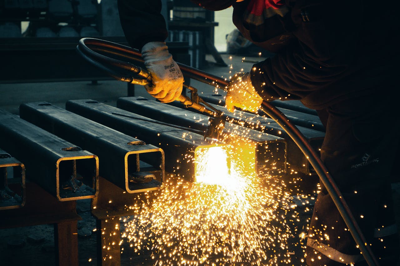Home A welder sparks metal beams indoors in an industrial factory setting.