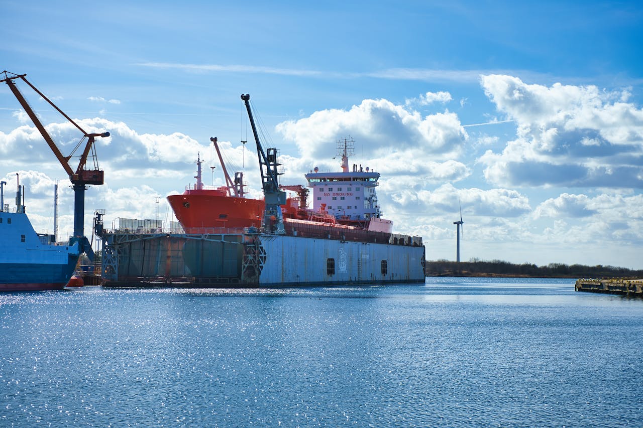 A vibrant scene of an industrial port featuring an oil tanker and cranes under a clear blue sky.