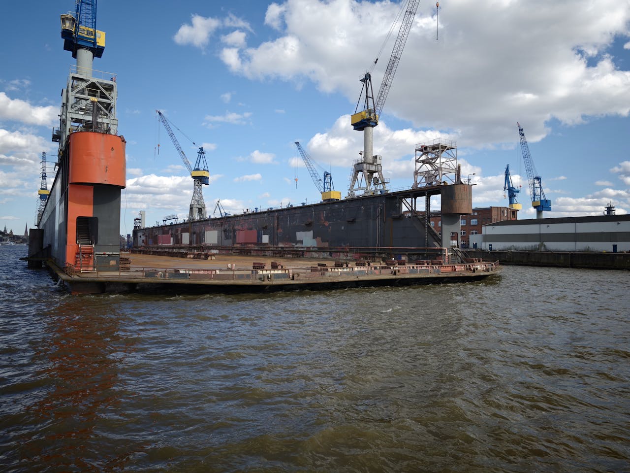 A shipyard featuring a docked vessel and multiple cranes under a bright blue sky.